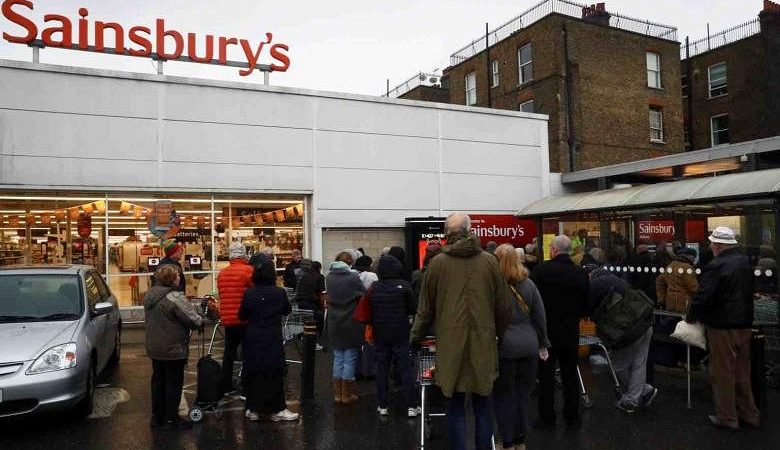 Menjelang penutupan London yang diharapkan, pembeli mengantri di tengah hujan di luar supermarket