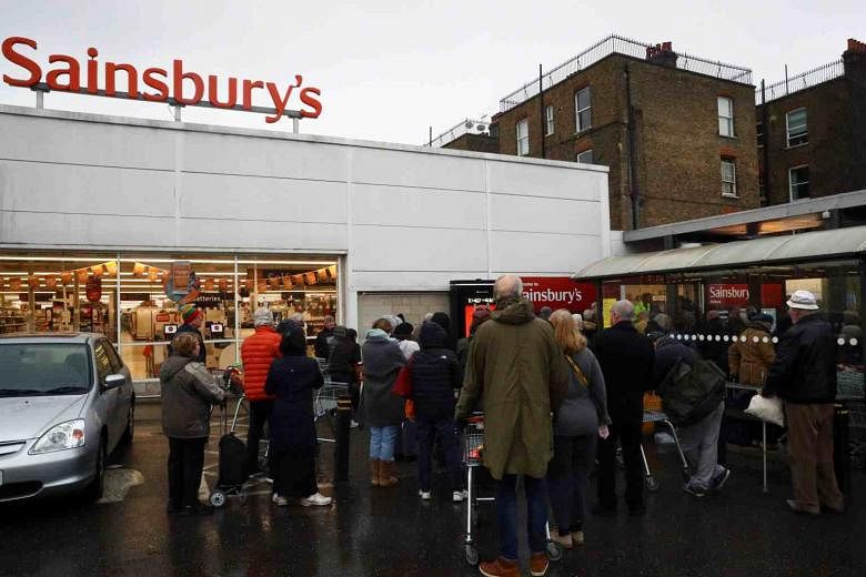 Menjelang penutupan London yang diharapkan, pembeli mengantri di tengah hujan di luar supermarket